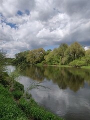 spring tranquil landscape with river, sky, clouds and reflection