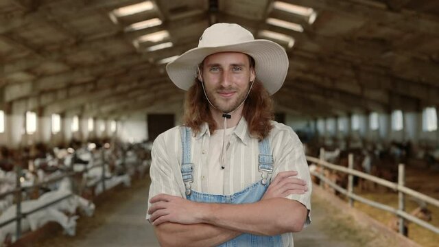 Positive male farmer in uniform standing at ranch with goats