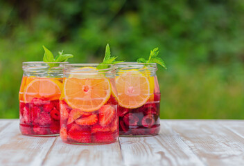 drink from berries, lemon and mint in jars on a table in the garden. summer refreshing lemonade.