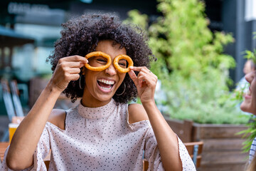 young and smiling African descending woman wearing fried onion rings as eyeglasses, funny and...