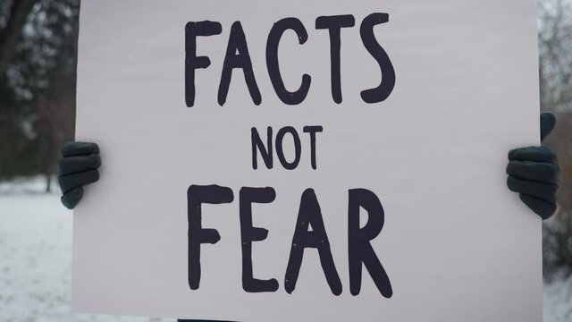 A Person Is Taking Part In A Peaceful Protest Outside. Holding A Poster Which Says Facts Not Fear. Demanding The Media To Stop Spreading Misinformation And Fake News. Cold Weather. Winter Park. Picket