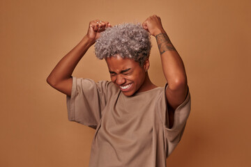 Excited joyous young cute African American woman raises clenched fists, stands without make up...