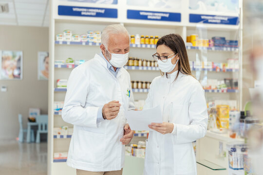 Colleague advice. Documentation and paper work in pharmacies during corona virus. A senior pharmacist explains the documentation in the pharmacy to a young pharmacist They wear uniforms and face masks