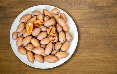 Pecan nuts ( Carya illinoinensis ) on white plate on modern wooden surface.