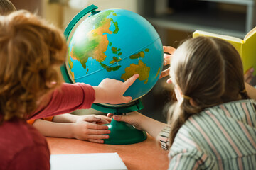 back view of blurred boy pointing at globe near kids and teacher