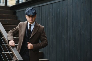 A man walks at city street in the image of an English retro gangster of the 1920s dressed in Peaky...