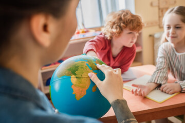selective focus of globe in hands of teacher near kids in montessori school
