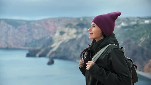 Happy backpacker brunette woman in hat contemplating beautiful sea landscape from mountain peak