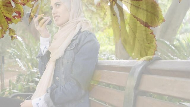 Animation of asian woman in hijab using smartphone over leaves