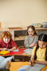 blurred teacher holding book near cheerful interracial kids during lesson
