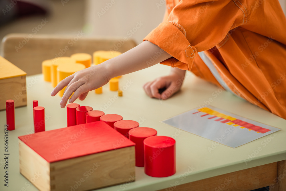 Wall mural cropped view of boy playing with red and yellow cylinders in montessori school