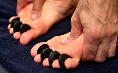 Close-up of a massage therapist performing an Ayurvedic acupressure on the feet using hot volcanic stones. Spa treatment concepts - obrazy, fototapety, plakaty