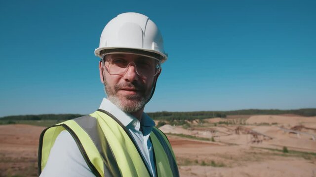 Portrait happy sand quarry worker engineer, male caucasian foreman in safety wear and hardhat looking at camera and smiling. Positive industrial worker, mining project specialist on sunny day