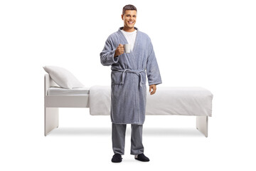 Full length portrait of a man in a bathrobe holding a cup in front of a bed - obrazy, fototapety, plakaty