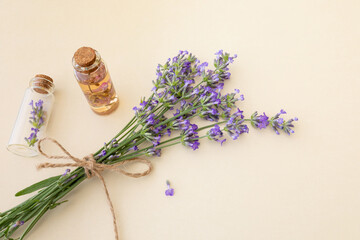 Obraz na płótnie Canvas Bouquet of blooming lavender and small glass bottles with essential lavender oil and flowers on beige background. Botanical cosmetics concept