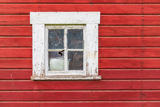 Window on the wall of an old red barn.