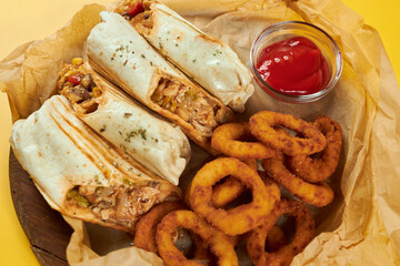 mexican burritos and onion rings with sauce on craft paper and yellow background