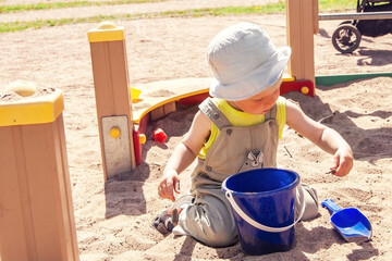 A small child plays in the sandbox, builds castles from sand. Children's playground in the city in summer.