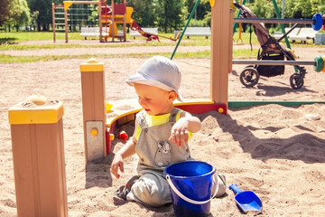 A small child plays in the sandbox, builds castles from sand. Children's playground in the city in summer.