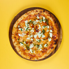 rustic pizza with feta cheese and herbs on wooden board and yellow background