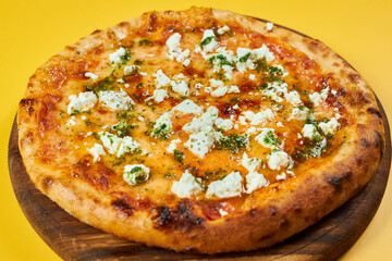 rustic pizza with feta cheese and herbs on wooden board and yellow background