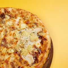rustic pineapple and chicken pizza on wooden board and yellow background