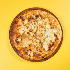 rustic pineapple and chicken pizza on wooden board and yellow background