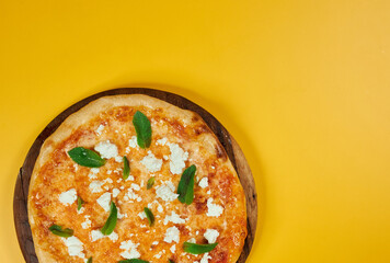 rustic pizza with feta cheese and herbs on wooden board and yellow background
