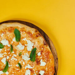 rustic pizza with feta cheese and herbs on wooden board and yellow background