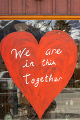 Red painting of a heart with We are in this together text on a window of the storefront 