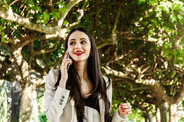 Caucasian young woman with executive wears and makeup, calling and talking on the phone in the park