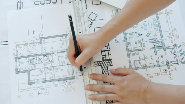 Top view of female hands architect drawing building plan with pencil concentrated on blueprint. Professionals at work and business activities concept.