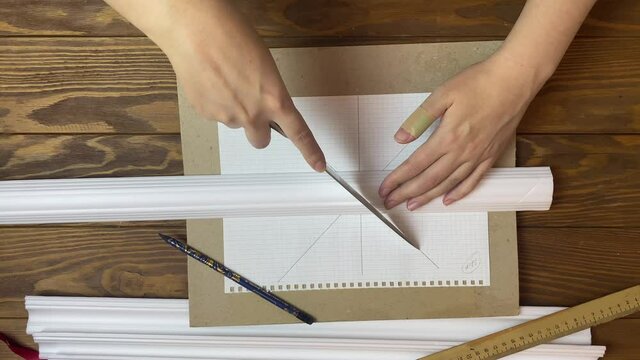 Women's hands cut molding with kitchen knife. On sketched notebook woman trims ceiling skirting board. Interior designer workplace. Diy handicraft.