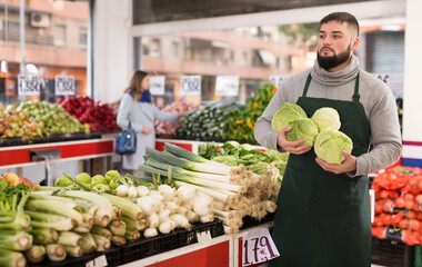 Male shop assistant lays fresh cabbage on counter in grocery shop. High quality photo
