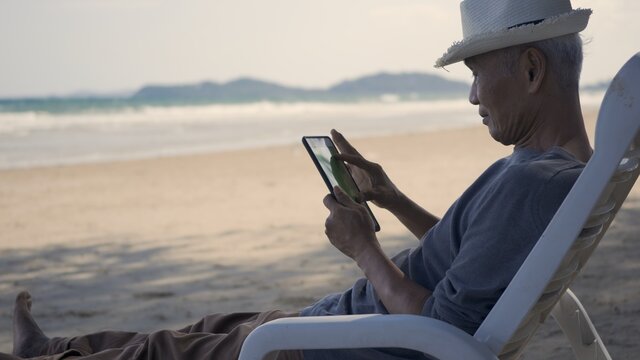 Senior man sitting on chairs enjoying time on beach travel vacation using tablet computer, Romantic elderly enjoy Travel summer vacation, plan life insurance at retirement concept