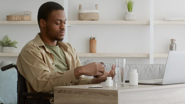 Disabled African American Man In Wheelchair Taking Pills At Home