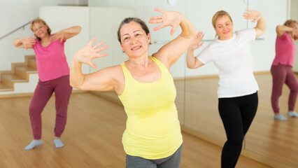 Portrait of active mature woman enjoying group training in dance studio