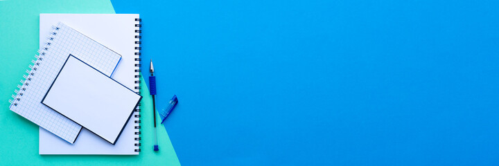 Banner of back to school concept. Stack of white spiral notebook, notepad and notepaper with pen, on a blue and aqua colorful background. School office supplies. Top view, flat lay