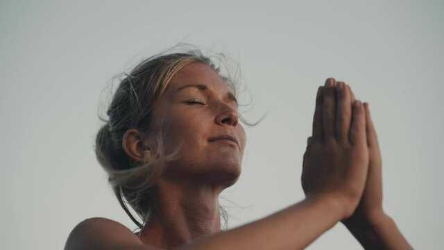 Woman practicing yoga sun salutation outside with wind blowing hair, Namast&eacute;