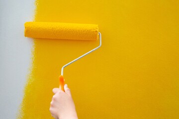 Woman roller painted yellow on the wall of the house herself