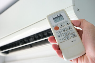 Man's hand using remote control open The air conditioner is cooled to 25 degrees Celsius in his bedroom. Health concepts and energy savings