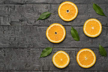 Bright green leaves and orange slices on a black wooden table. Space for the text. Flat lay.