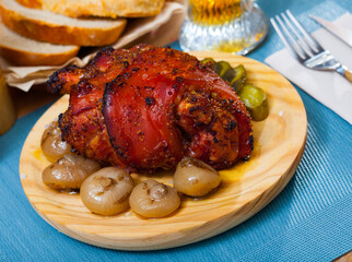 Appetizing spicy pork shank baked in beer garnished with marinated cucumbers and onions