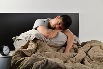 Depressed young Asian man sitting in bed cannot sleep from insomnia