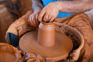 Closeup of male hands sculpting ceramics on potters wheel in pottery workshop