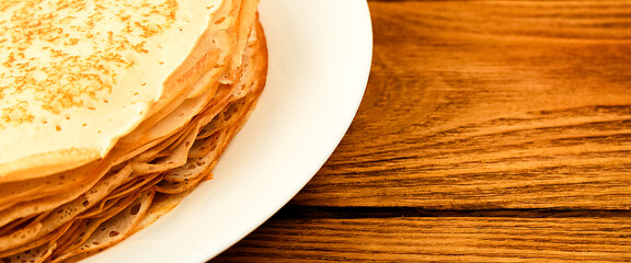 Pancakes on a plate on a wooden table. A large stack of fresh pancakes. Delicious healthy fresh pancakes. Place for advertising, logo, lettering, layout.
