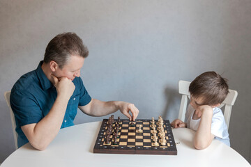 Dad and son are playing a board game of chess. Time and games with children. Logic and strategy game