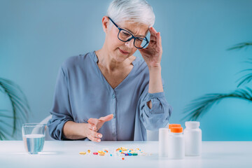 Confused senior woman looking at her medicines on the table. Medicine non-adherence concept.