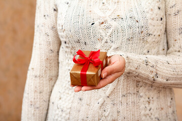 Woman holding a gift box tied with red ribbon in the hand.