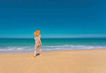 Fototapeta na wymiar Young beautiful girl in beige dress running on the the sandy beach near the waves. High quality photo